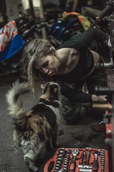 ガレージに長い髪の美しい女の子がバイクを修理します — ストック写真