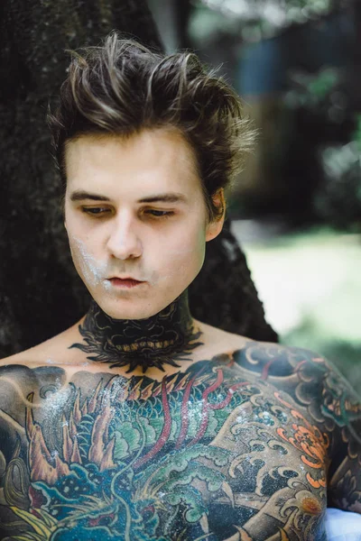 Genç, yakışıklı, dövmeli bir adam kahvaltısını yapıyor açık havada bahçede, açık havada, kahvaltıda çörek ve kahve içiyor..