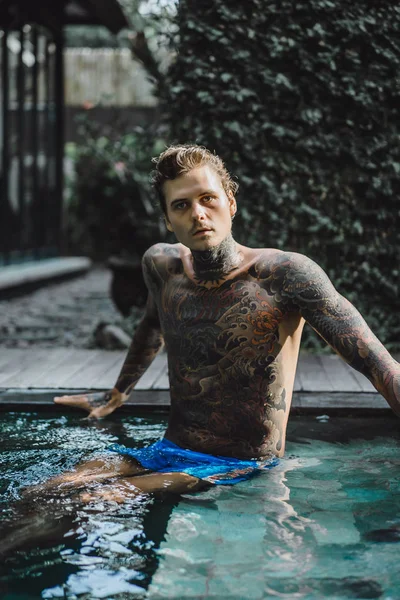 Açık Yüzme havuzunda dinlenme dövmeler genç yakışıklı adam. Dövmeli bir adam havuzda eğleniyor. Bali, Endonezya