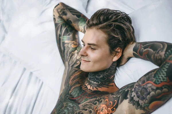 handsome young man in tattoos relaxing in bed