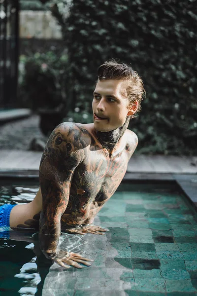 young handsome man in tattoos resting in the outdoor pool. A tattooed man in the pool is having fun. on bali, indonesia