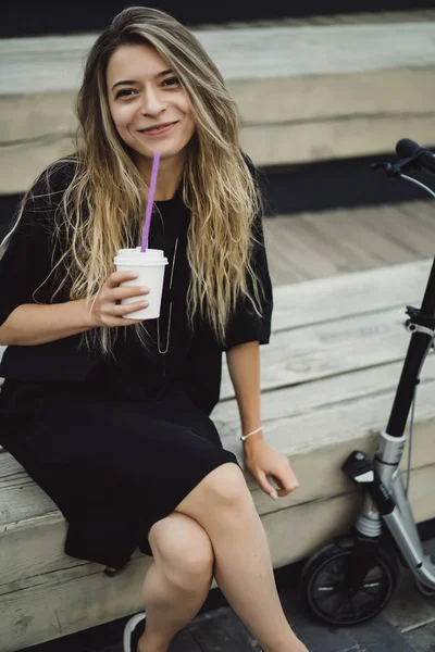 電動スクーターに長い髪を持つ若い女性 電気スクーターの女の子はコーヒーを飲む — ストック写真