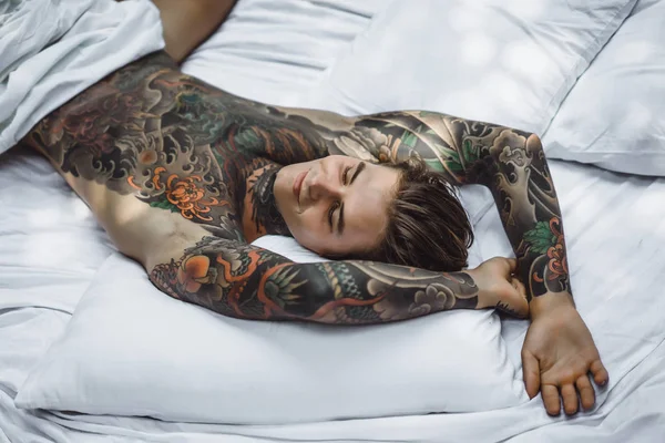 ベッドでリラックスしたタトゥーのハンサムな若い男 — ストック写真
