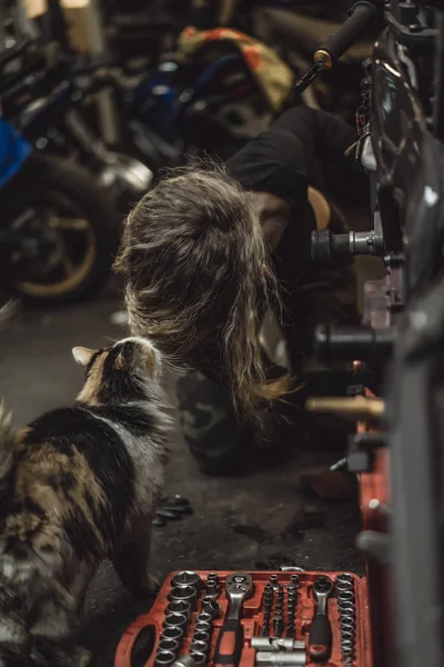 ガレージに長い髪の美しい女の子がバイクを修理します — ストック写真