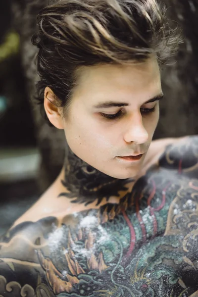 young handsome tattooed man having breakfast in bed in the open air outdoors in the garden, donuts and coffee for breakfast.