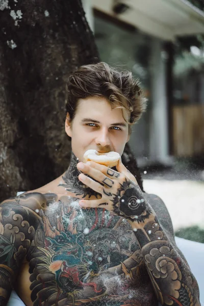 Молодой Красивый Татуированный Мужчина Завтракает Постели Открытом Воздухе Саду Пончики — стоковое фото