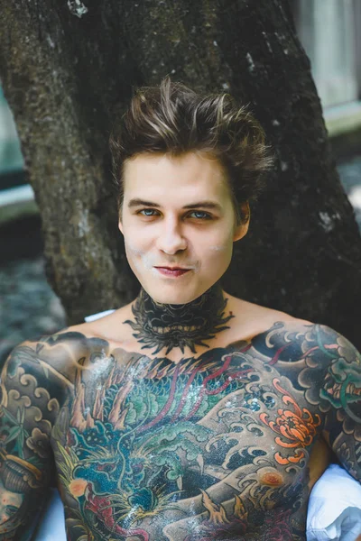 Genç, yakışıklı, dövmeli bir adam kahvaltısını yapıyor açık havada bahçede, açık havada, kahvaltıda çörek ve kahve içiyor..