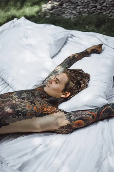 ベッドでリラックスしたタトゥーのハンサムな若い男 — ストック写真