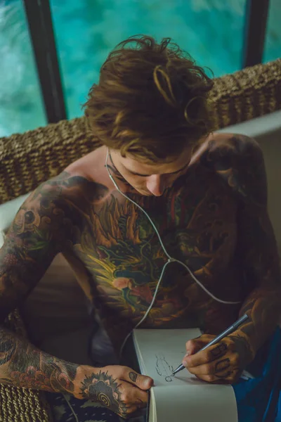 Giovane Tatuato Con Cuffie Ascolta Musica Disegna Una Matita Quaderno — Foto Stock