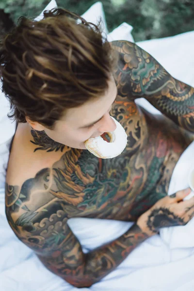 Jonge Knappe Getatoeëerde Man Ontbijten Bed Buitenlucht Tuin Donuts Koffie — Stockfoto