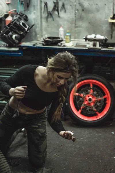 ガレージに長い髪の美しい女の子がバイクを修理します — ストック写真