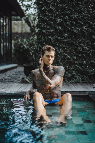 Açık Yüzme havuzunda dinlenme dövmeler genç yakışıklı adam. Dövmeli bir adam havuzda eğleniyor. Bali, Endonezya