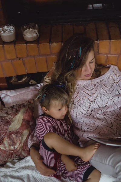 若い母親と息子は 暖炉のそばのおとぎ話の本を読んでいます — ストック写真