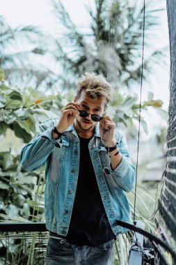 tropikal bir yerde, palmiye ağaçları ve yeşil, güneş gözlüklü bir arka plan üzerinde poz genç çekici adam