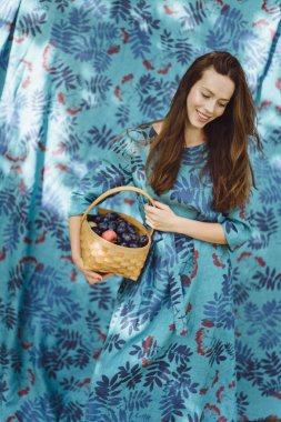 Elinde meyve, erik ve elma sepeti olan genç bir kadın..
