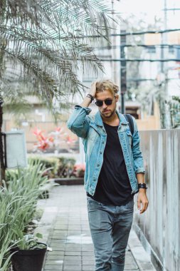 tropikal bir yerde, palmiye ağaçları ve yeşil, güneş gözlüklü bir arka plan üzerinde poz genç çekici adam