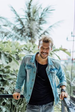 tropikal bir yerde, palmiye ağaçları ve yeşil, güneş gözlüklü bir arka plan üzerinde poz genç çekici adam