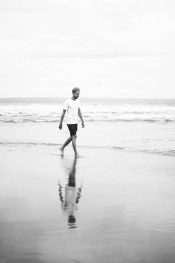 okyanus plaj boyunca kumlu bir plaj üzerinde yürüyen genç çekici adam