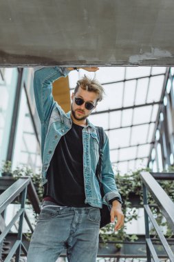 tropikal bir yerde, palmiye ağaçları ve yeşil, güneş gözlüklü bir arka plan üzerinde poz genç çekici adam