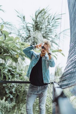 tropikal bir yerde, palmiye ağaçları ve yeşil, güneş gözlüklü bir arka plan üzerinde poz genç çekici adam