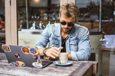 genç çekici iş adamı için bir dizüstü bilgisayar, bir kafe eserlerinde kahve içiyor.