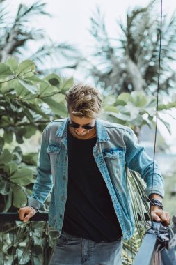 tropikal bir yerde, palmiye ağaçları ve yeşil, güneş gözlüklü bir arka plan üzerinde poz genç çekici adam