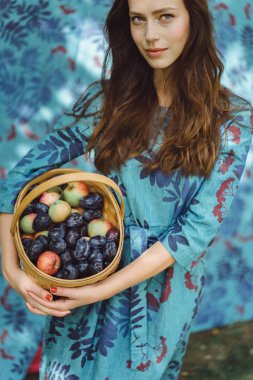 Elinde meyve, erik ve elma sepeti olan genç bir kadın..