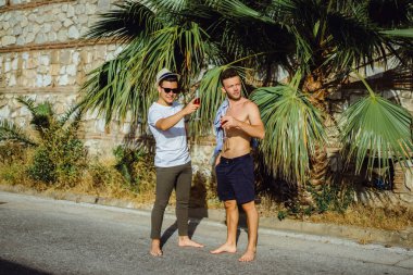 İki arkadaş, tropik yeşilliğin arka planında şampanya kadehleri olan genç adamlar.