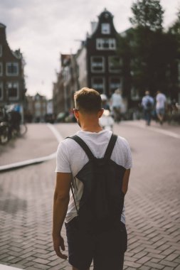 Bir insan bir sırt çantası ile Amsterdam sokaklarında yürüyor.