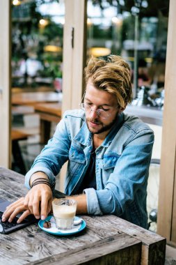 genç çekici iş adamı için bir dizüstü bilgisayar, bir kafe eserlerinde kahve içiyor.