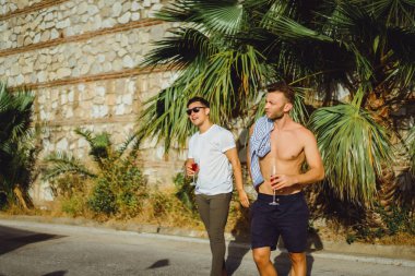 İki arkadaş, tropik yeşilliğin arka planında şampanya kadehleri olan genç adamlar.