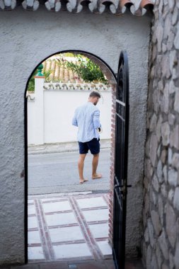 çizgili gömlekli, hasır şapka giyen bir adam, küçük bir İspanyol kasabasının sokaklarında yürüyor..