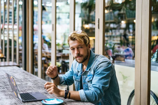 genç çekici iş adamı için bir dizüstü bilgisayar, bir kafe eserlerinde kahve içiyor.