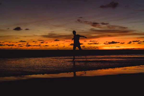 夕暮れ時の海の海岸に人々 男が夕日を背にジャンプします — ストック写真