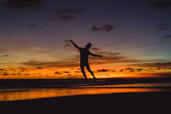 夕暮れ時の海の海岸に人々 男が夕日を背にジャンプします — ストック写真