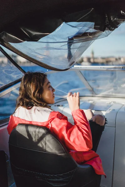 beautiful young woman in a red cloak drinking champagne on a yacht.