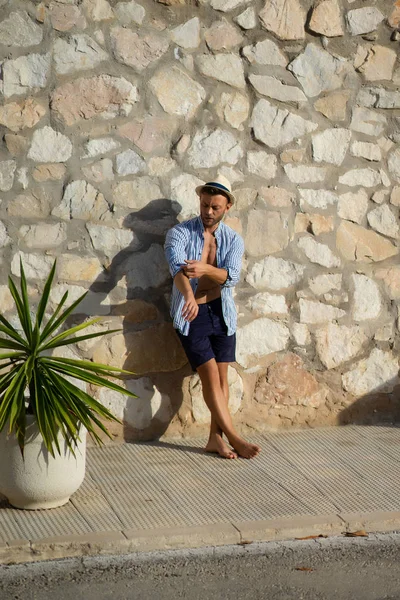 ストライプのシャツを着た男が麦わら帽子をかぶり スペインの小さな町の通りを歩く — ストック写真