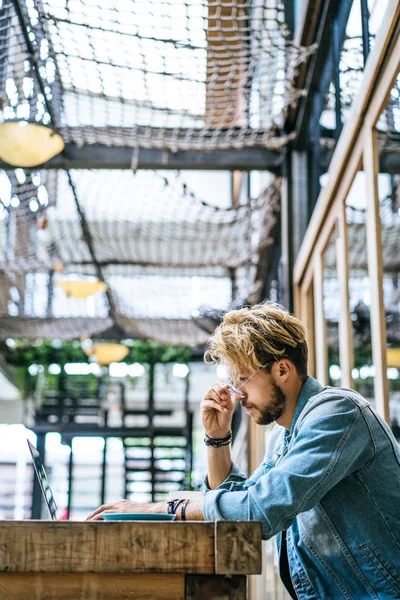 genç çekici iş adamı için bir dizüstü bilgisayar, bir kafe eserlerinde kahve içiyor.