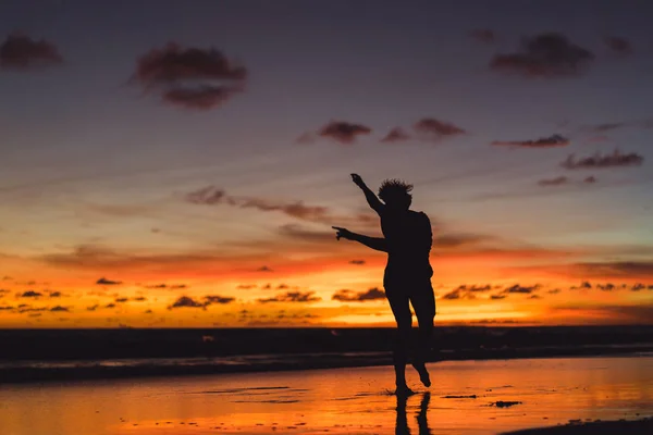 夕暮れ時の海の海岸に人々 男が夕日を背にジャンプします — ストック写真