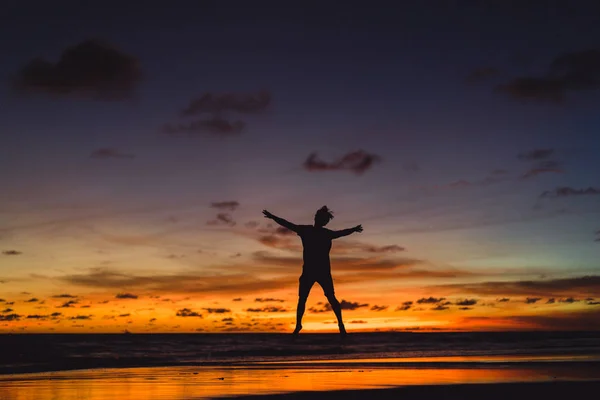 夕暮れ時の海の海岸に人々 男が夕日を背にジャンプします — ストック写真