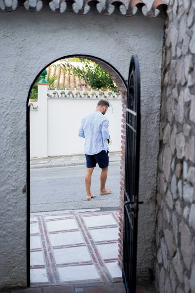 çizgili gömlekli, hasır şapka giyen bir adam, küçük bir İspanyol kasabasının sokaklarında yürüyor..