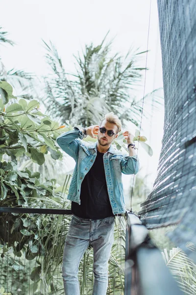 tropikal bir yerde, palmiye ağaçları ve yeşil, güneş gözlüklü bir arka plan üzerinde poz genç çekici adam