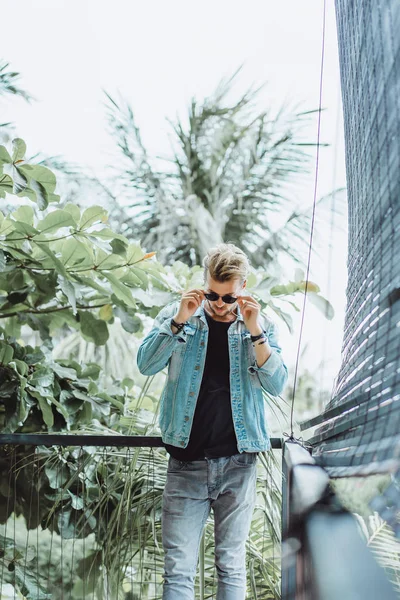 tropikal bir yerde, palmiye ağaçları ve yeşil, güneş gözlüklü bir arka plan üzerinde poz genç çekici adam