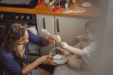 Mutfakta küçük çocuk anne pişirmek için yardımcı olur. Çocuk pişirme ilgilenmektedir.