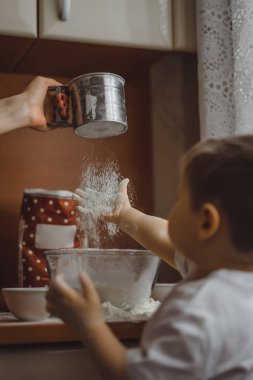 Mutfakta küçük çocuk anne pişirmek için yardımcı olur. Çocuk pişirme ilgilenmektedir.