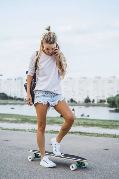 bir smartphone kullanarak bir kaykay ile uzun saçlı kız. Sokak, aktif spor