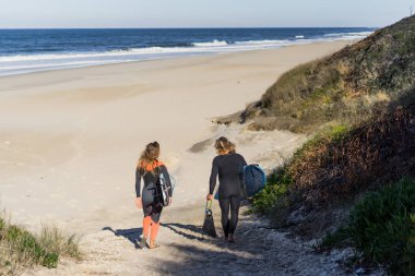 Erkek ve kadın sörf tahtaları ile okyanusa gidin. Erkek ve kız sörf, Portekiz, Nazar gidin. Islati takım elbiseyle sörf.