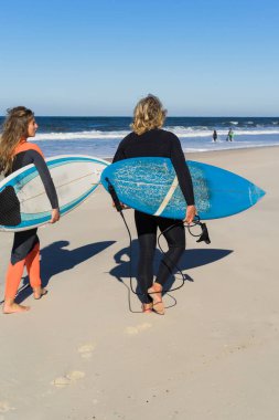 Erkek ve kadın sörf tahtaları ile okyanusa gidin. Erkek ve kız sörf, Portekiz, Nazar gidin. Islati takım elbiseyle sörf.