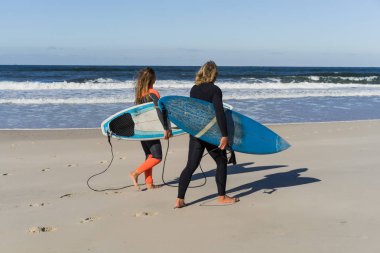 Erkek ve kadın sörf tahtaları ile okyanusa gidin. Erkek ve kız sörf, Portekiz, Nazar gidin. Islati takım elbiseyle sörf.