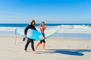 Erkek ve kadın sörf tahtaları ile okyanusa gidin. Erkek ve kız sörf, Portekiz, Nazar gidin. Islati takım elbiseyle sörf.